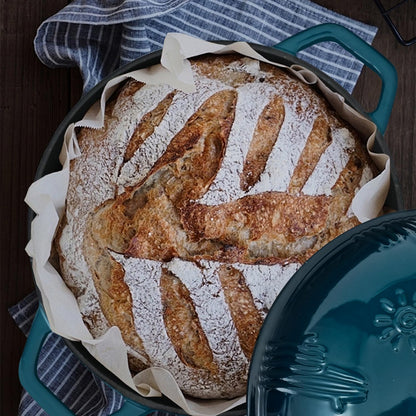 Baked bread in a round baking dish with a blue lid on a wooden surface.