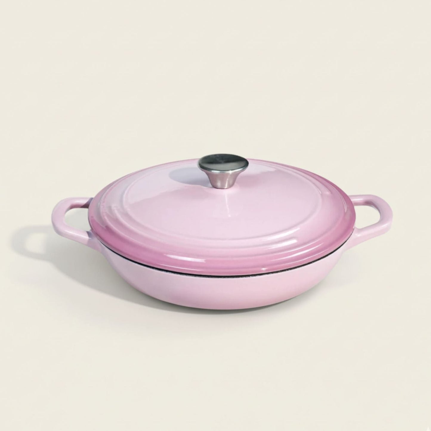 Pink enameled cast iron shallow casserole cookware with lid on a light beige background
