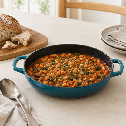 Dark cyan enamelled cast iron shallow casserole with side handles, filled with beans