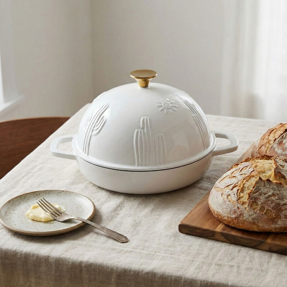 White enamelled dutch oven cloche with decorative lid on a table with bread and butter.