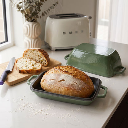 Sage green (enamelled) oval bread oven with lid and base tray, with a sliced loaf
