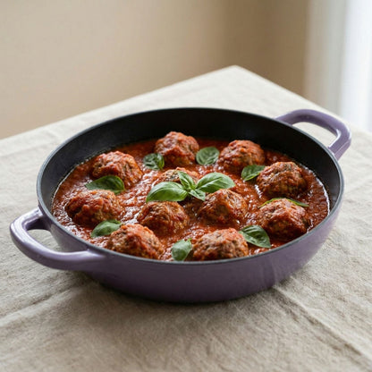 Purple skillet with meatballs and tomato sauce on a beige surface
