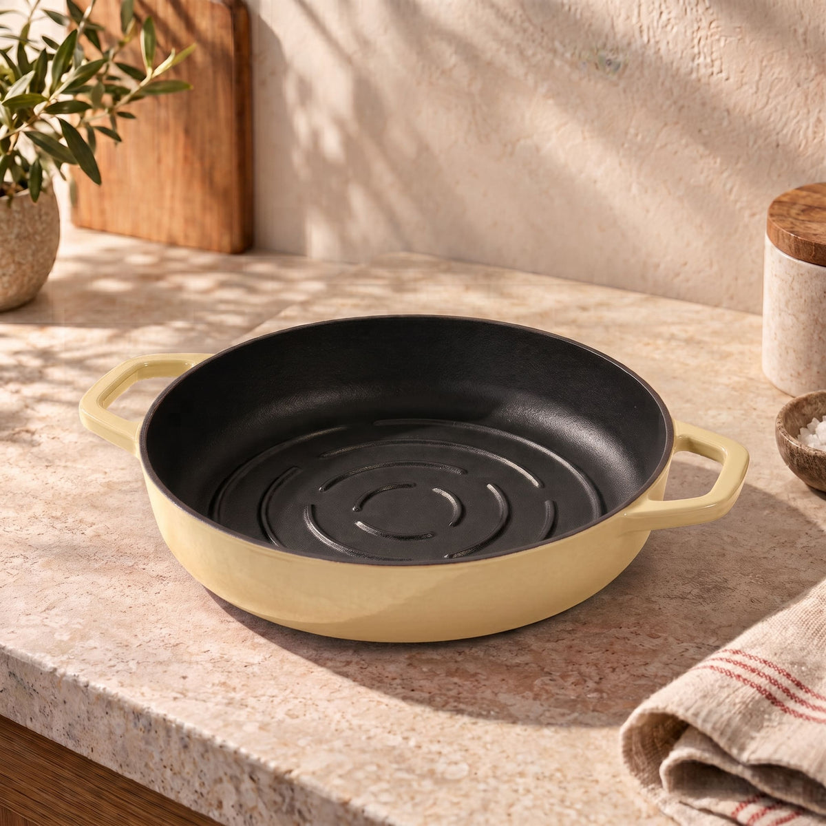 A round cast iron bread pan with a butter yellow exterior and a black interior, shown on a beige stone countertop in a kitchen setting.