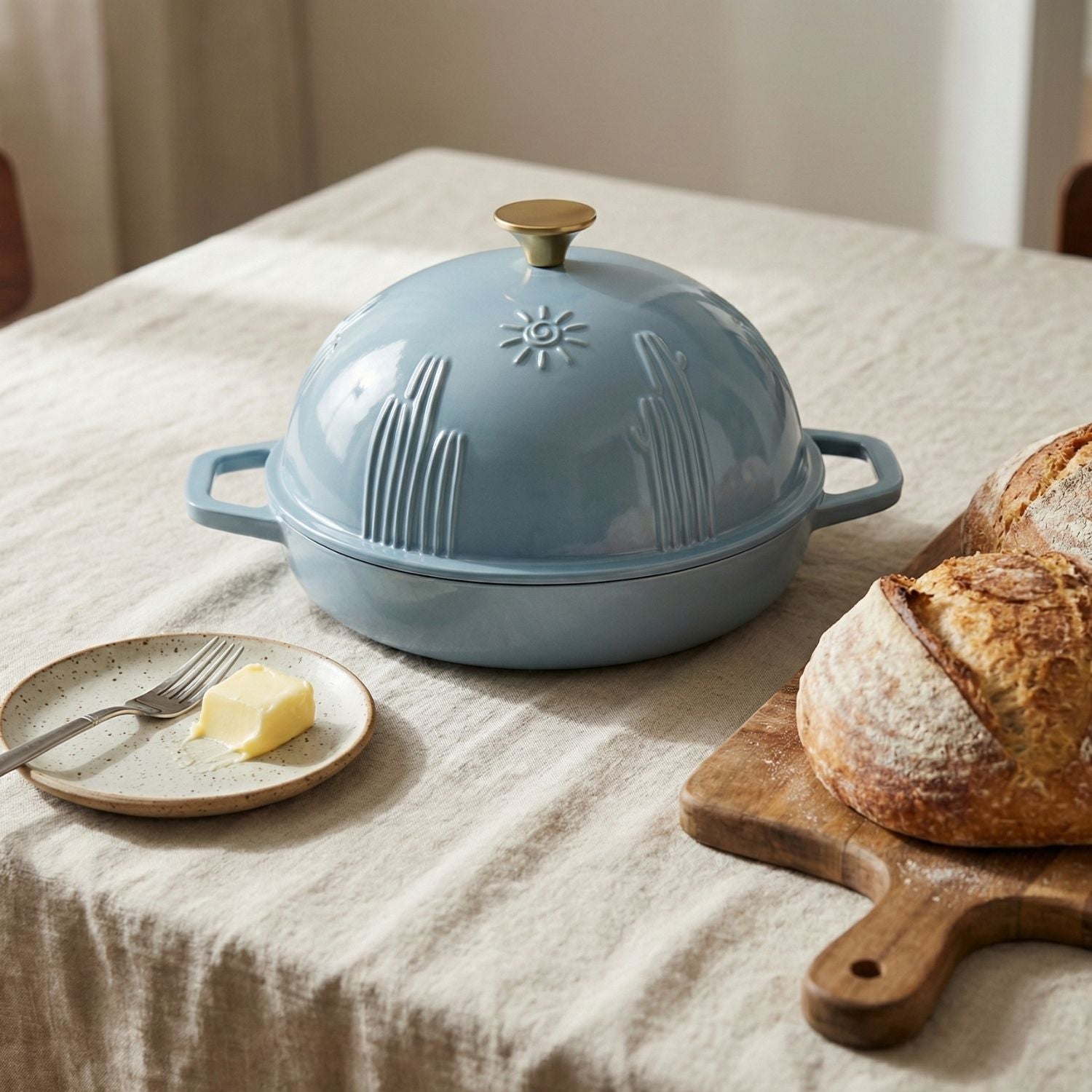Blue cast iron bread proofing dome on a table with bread and butter