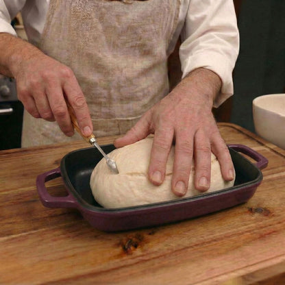 Plum purple oval bread oven tray holding dough as a baker shapes the loaf. Plum Purple (enamelled)