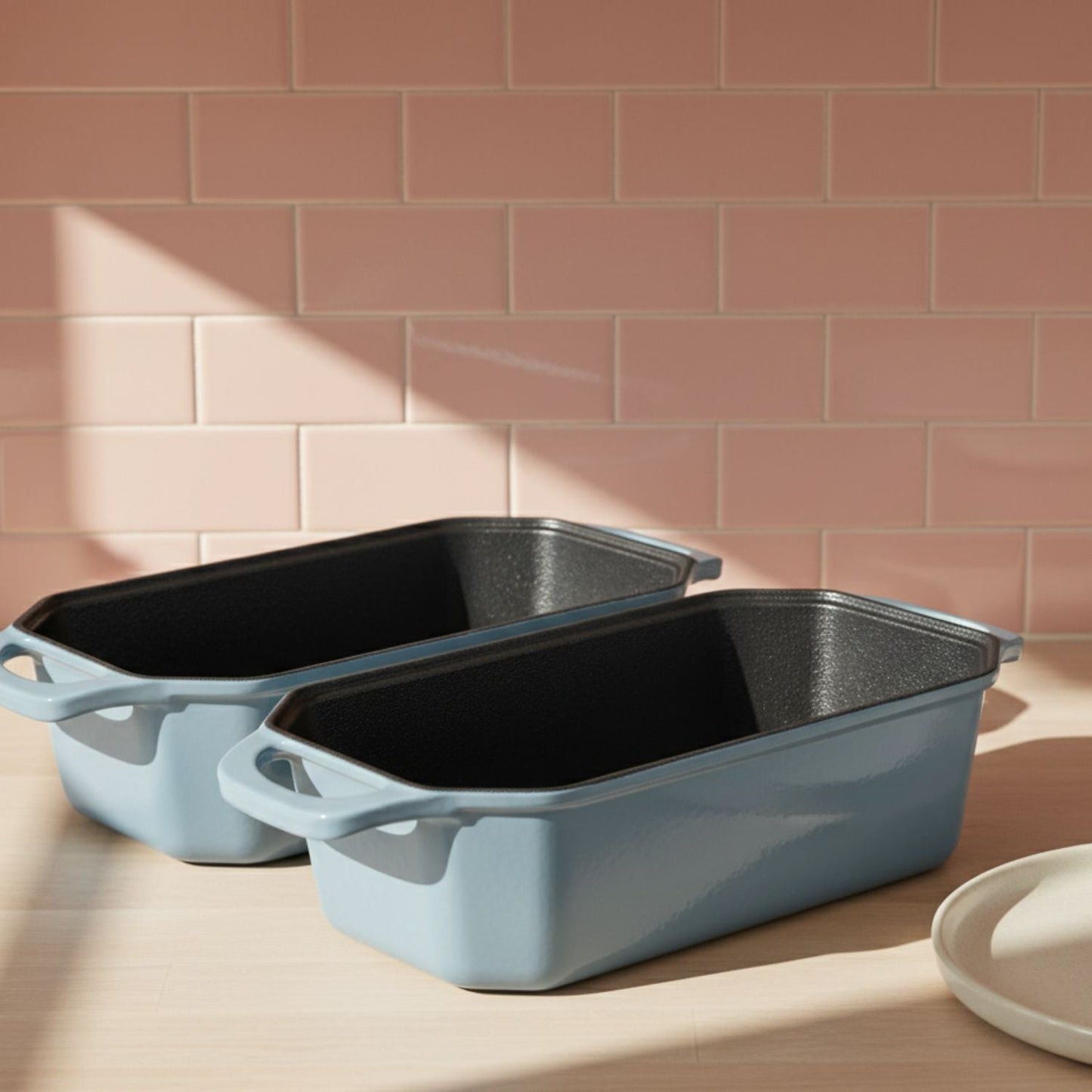 Two blue rectangular baking dishes on a wooden surface with a pink tiled wall background.
