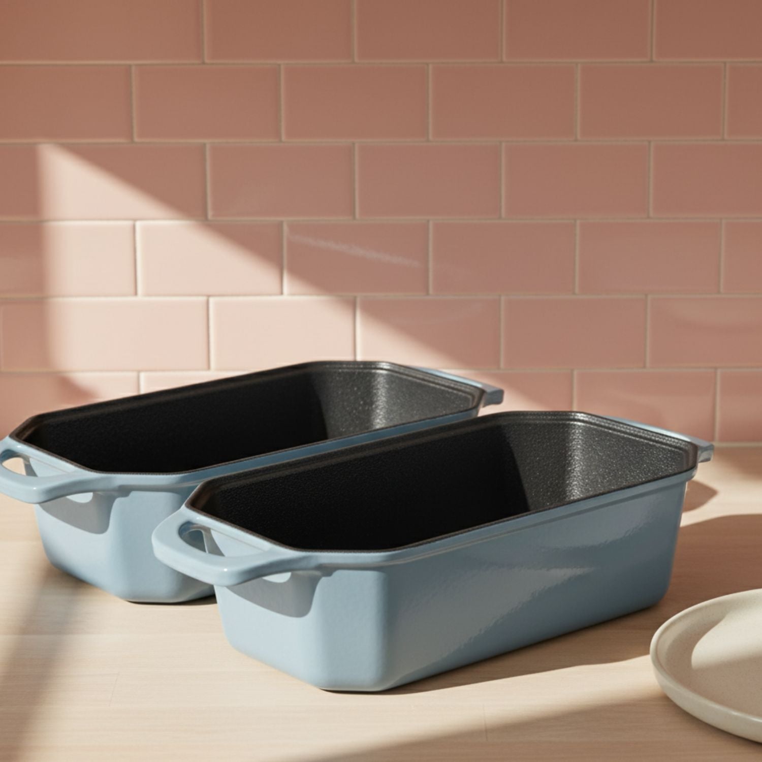 Two blue rectangular baking dishes on a wooden surface with a pink tiled wall background.