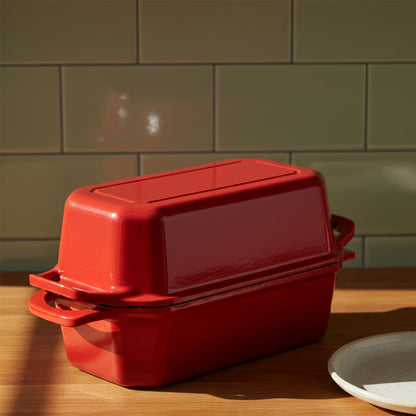Red cast iron bread pan nz baking dish with lid on a wooden surface against a green tiled wall.