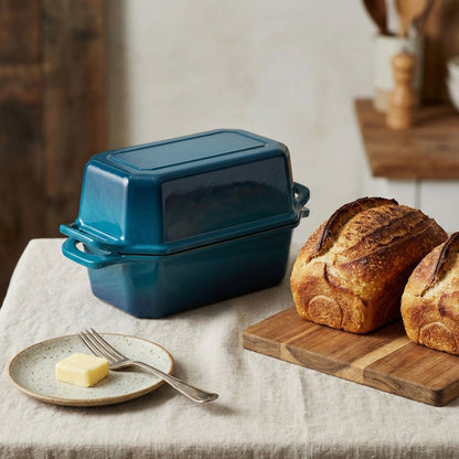 Blue cast iron bread loaf pan on a kitchen counter with bread and butter.