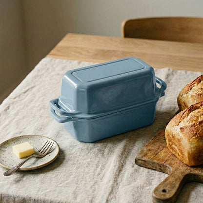 Blue cast iron loaf pan on a wooden table with bread and butter.