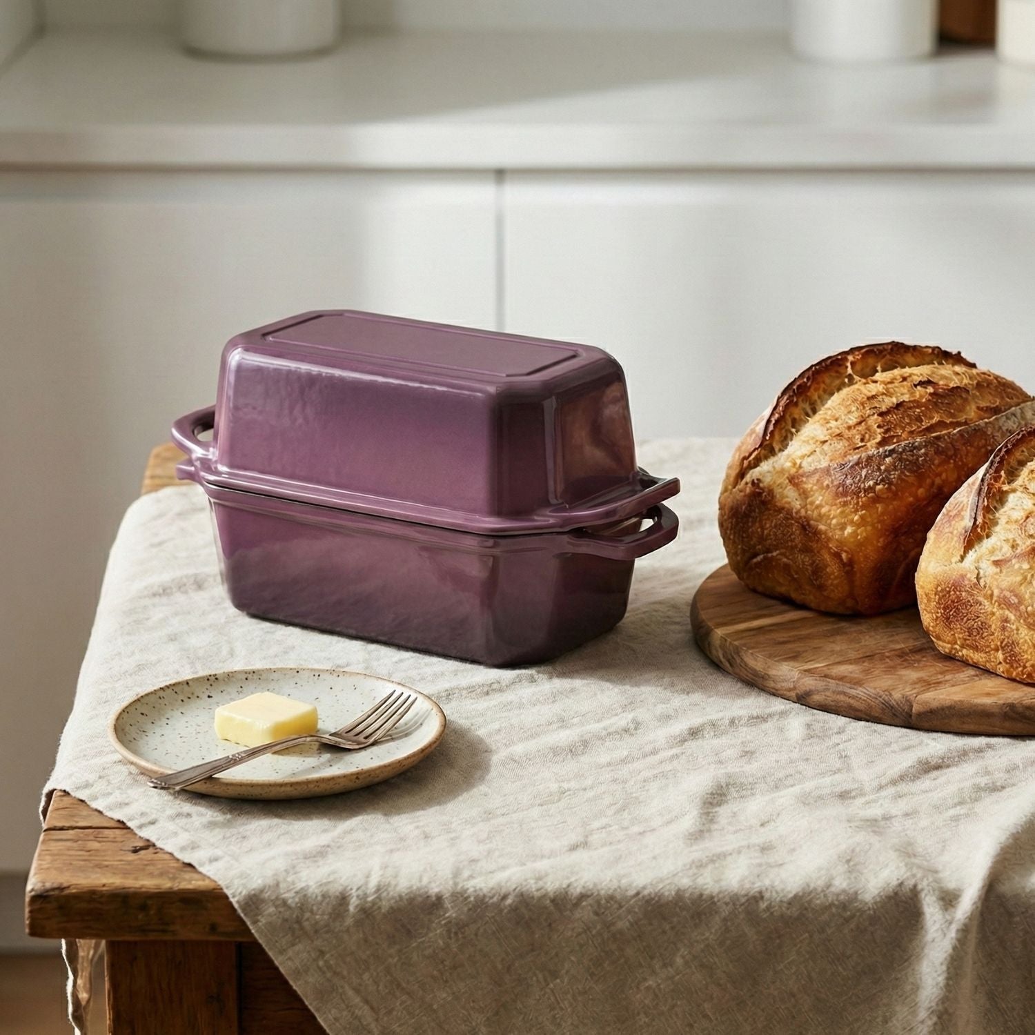 Purple cast iron bread pan on a kitchen counter with bread and butter.