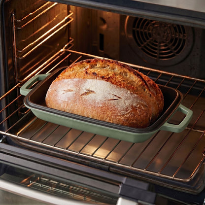 Sage green (enamelled) oval bread oven in an oven, with a baked loaf on the tray