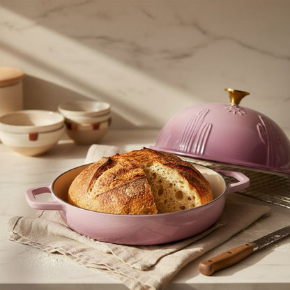 Loaf of bread in a pink baking dish with a pink lid on a marble surface.