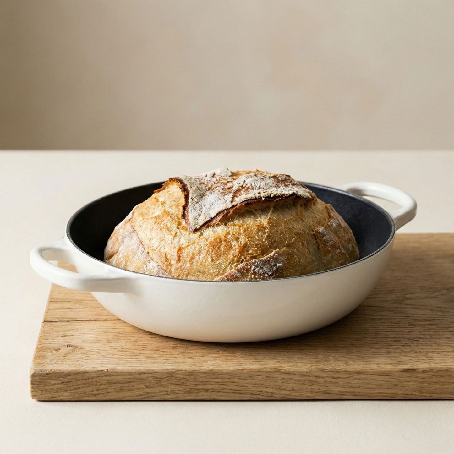 Loaf of bread in a white dutch oven casserole dish on a wooden board with a beige background