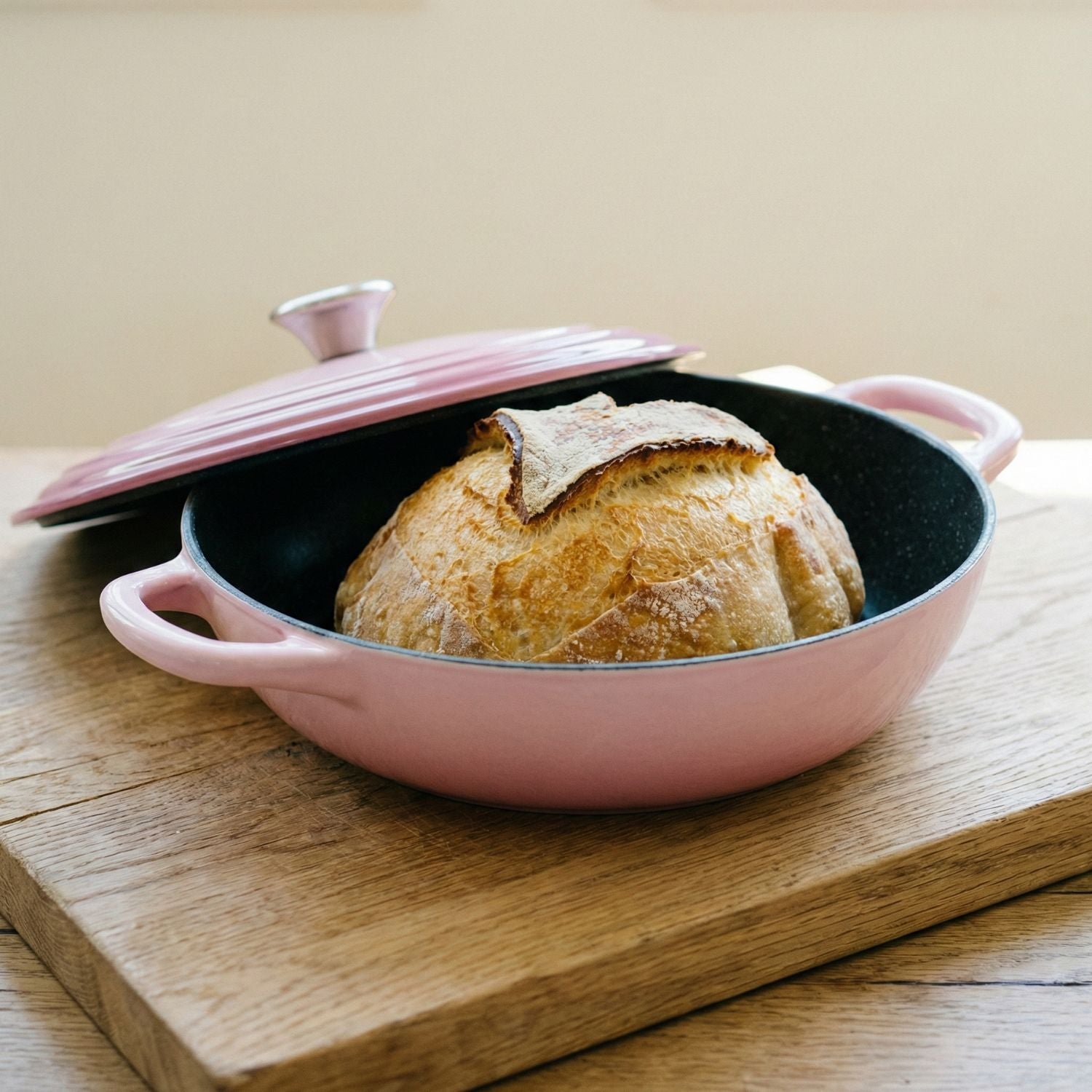 Pink ceramic bread loaf dish with a loaf of bread on a wooden surface