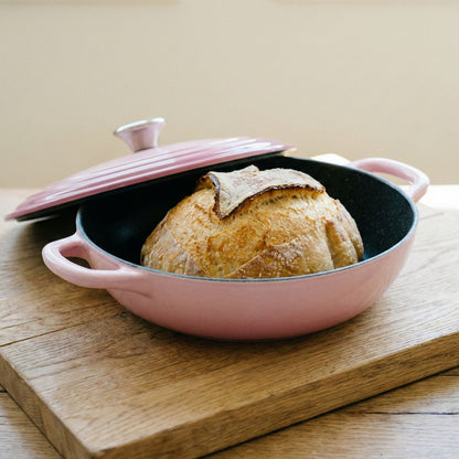 Pink ceramic bread loaf dish with a loaf of bread on a wooden surface