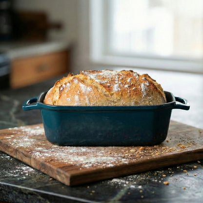 Loaf of bread in a blue baking dish on a wooden cutting board in a kitchen.